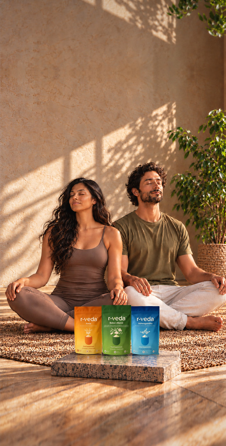 Two people meditating cross-legged in warm sunlight beside r-veda Amla, Baba’s Blend and Ashwagandha pouches on a stone plinth